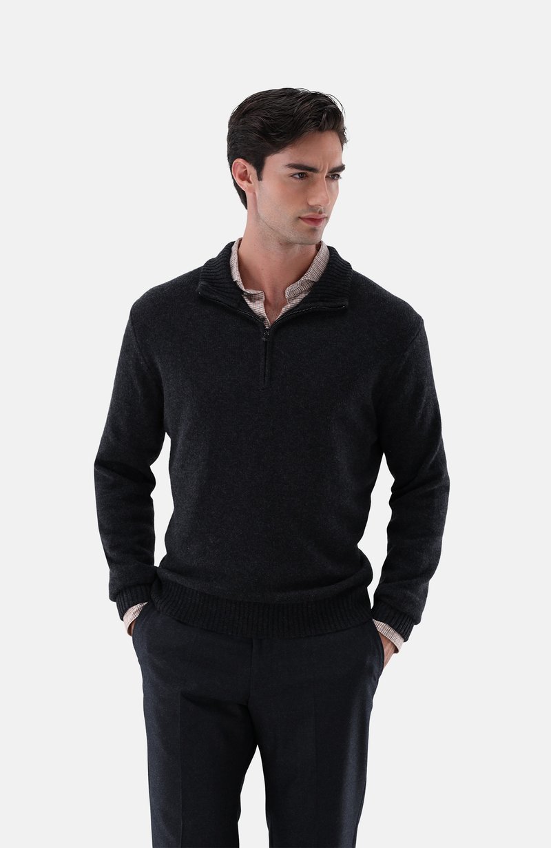 Dunkler Pullover mit Reißverschlusskragen, ribbeltem Saum und strukturiertem Stoff. Getragen über einem gemusterten Hemd, kombiniert mit dunklen Hosen.