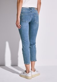 Vaqueros de denim de color azul claro con un corte corto, diseño ajustado, bolsillos traseros y detalles de costura. Combinados con zapatillas blancas.