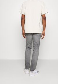 Lichtbeige katoenen T-shirt, casual pasvorm, gecombineerd met lichtgrijze jeans. Draagt een paar witte sneakers met grijze en blauwe accenten.