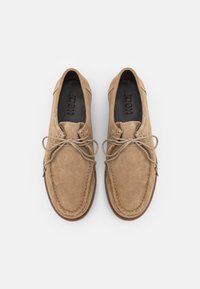 Zapatos de ante beige con puntera redondeada, costuras en contraste y suela de goma plana. Cuentan con cordones atados y una plantilla negra suave.
