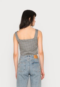 Top cropped em padrão de gingham preto e branco com alças largas e costas quadradas, combinado com jeans de cintura alta azul claro com dois bolsos traseiros.