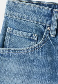 Gros plan sur un jean en denim bleu montrant la poche avant, la petite poche à monnaie, les passants de ceinture et les détails de coutures avec rivets métalliques.