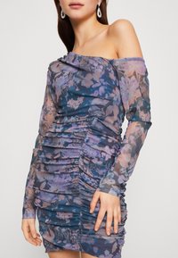 Sukienka bez ramiączek z przezroczystej tkaniny w niebiesko-fioletowy kwiatowy wzór. Posiada marszczone detale oraz długie rękawy.