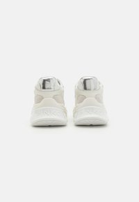 Sneakers bianchi con accenti metallici, superfici testurizzate e una suola pronunciata; presenta il marchio sul tallone. Vista posteriore mostrata.