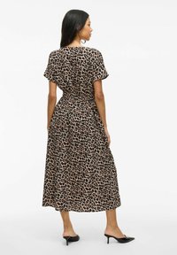 Robe maxi en imprimé léopard avec manches courtes, taille cintrée, tissu fluide et fentes sur les côtés, associée à des mules à talons noirs.