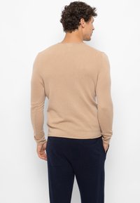 Hellbraunes Sweatshirt mit langen Ärmeln, geripptem Textur und rundem Halsausschnitt, kombiniert mit navyfarbigen Hosen mit Taschen.