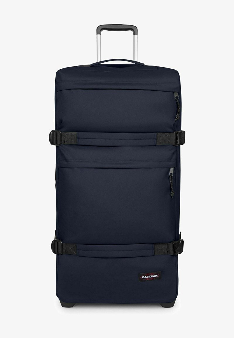 Valise à roulettes bleu marine avec poignée extensible, deux sangles de compression noires, poches avant zippées et logo Eastpak en bas à droite.
