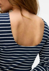 Mörkblå randig topp med ribbad textur, med en bred rundad nedringning på ryggen. Hud synlig under nedringningen. Mjuk tyg.