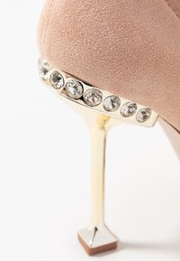 Rosa mockaskinn högklackad sko med en glänsande metallisk guld stilettklack. Klacken har en rad klara rhinstenar för extra detalj.