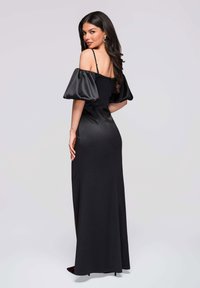Robe noire en satin, décolleté Bardot avec manches bouffantes, corsage ajusté et fente haute. Texture lisse et longueur jusqu'aux chevilles.