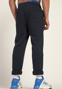 Navy sweatpants met een blauwe elastische tailleband, voorzien van opgerolde boorden en twee achterzakken. Het gestructureerde materiaal zorgt voor een comfortabele pasvorm.