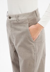Szare spodnie cordurowe z bocznymi kieszeniami, teksturowana tkanina oraz zapięcie na guzik w pasie. Umieszczone na wysokości bioder modelki.