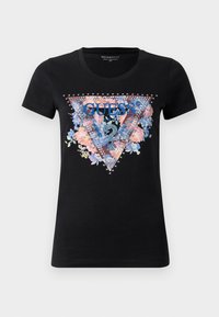 Svart kortermet t-skjorte med blomstertriangel-design, blå "GUESS"-logo, spørsmålstegn-emblem og sølvnitter rundt trykket.