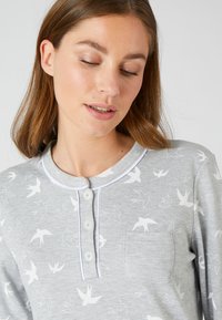 Top grigio a maniche lunghe con colletto arrotondato, decorato con motivi di uccelli bianchi, una tasca sul petto e chiusura con bottoni bordata a contrasto.