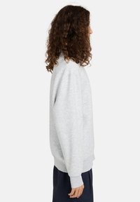 Grijze sweatshirt met een ronde hals, lange mouwen en geribbelde manchetten. Eenvoudig ontwerp en zachte textuur, gedragen over donkere broeken.