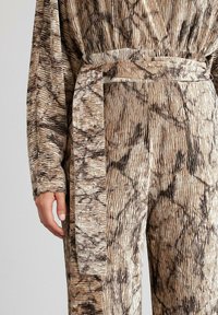 Tela texturizada y patterned en tonos de marrón y beige, con un cinturón y mangas anchas, presentando un diseño ondulado y arrugado en todo su recorrido.