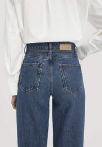 Hoge taille blauwe spijkerbroek met een relaxte pasvorm, voorzien van twee achterzakken en een tan leren logo badge op de tailleband.