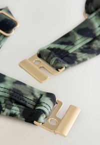 Bretele reglabile cu un model de camuflaj verde și negru. Prezintă accesorii metalice aurii și o textură netedă a țesăturii.