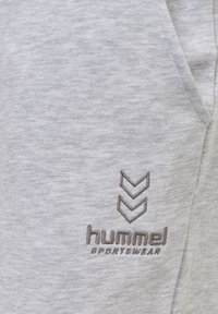 Grå sweatshirt tyg med en texturerad yta. Har en broderad logotyp i brunt och tre chevron detaljer. Designen inkluderar sidfickor.