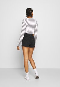 Randig långärmad skjorta med figurnära design, i kombination med svarta denimshorts med fransade kanter. Vita sneakers fulländar looken.