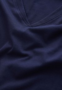 Gros plan sur un tissu bleu marine montrant un décolleté en V avec des coutures visibles et des plis doux dans le textile.