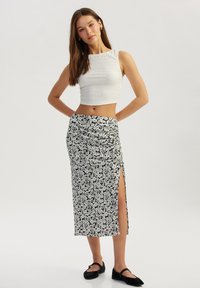 Witte cropped top van textuurstof; zwart-witte bloemenpatroon wikkelrok met een zijsplit. Gemaakt met zwarte platte schoenen.