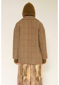 Manteau en mélange de laine marron avec un motif à carreaux, doté d'un col en V, d'une coupe oversize et d'une capuche en tricot, associé à une jupe fluide à motif.