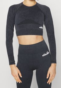 Schwarzes, langärmliges Crop-Top mit strukturiertem Netzdetail und geripptem Saum; kombiniert mit hochtaillierten, schwarzen Leggings mit glatter Oberfläche.