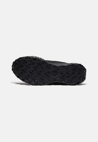 Semelle de chaussure de sport noire dotée d'une surface en caoutchouc texturé avec des crampons multidirectionnels pour une meilleure traction et durabilité.