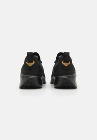 Black athletic shoes with a textured fabric upper, a smooth black rubber outsole, and a contrasting gold accent on the heel tab.