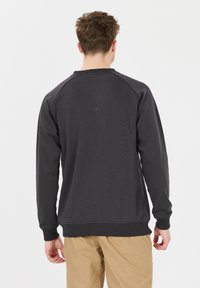 Sweat-shirt gris foncé avec des manches raglan et des poignets côtelés. Il présente un col rond et un tissu texturé. Porté avec un pantalon beige.