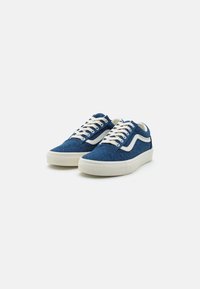 Blue denim sneakers with white accents, flat laces, and a rubber sole. Features a textured upper and classic Vans stripe design.