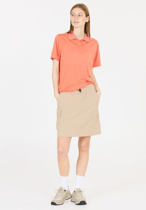 Korallenfarbendes Poloshirt mit kurzen Ärmeln, beiger Cargo-Rock mit Seitentaschen und hellgraue Turnschuhe mit weißen Socken.
