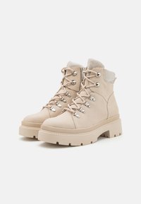 Bottes beige à la cheville avec une finition texturée, dotées de quincaillerie en argent et de lacets, d'une semelle en caoutchouc épaisse et d'un détail en mesh sur le dessus.