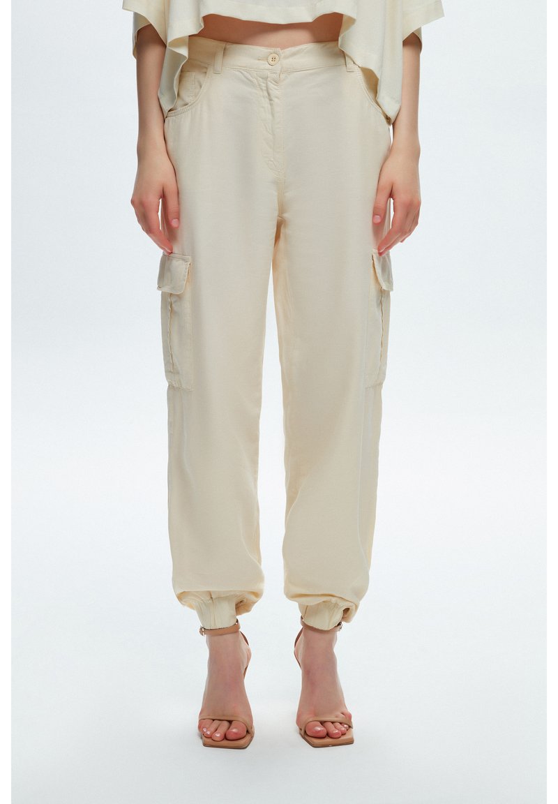 Beige cargo shorts hebben een relaxte pasvorm met elastische boorden, zijzakken en een knoopsluiting bij de tailleband. Soepele stoftextuur.
