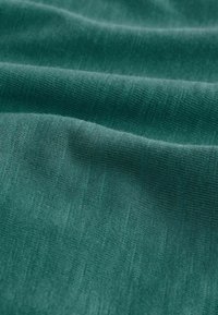 Tessuto color teal con una texture morbida, caratterizzato da linee sottili e una superficie liscia. Il materiale appare leggero e leggermente elastico.
