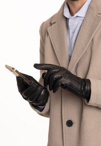 Schwarze Lederhandschuhe mit glatter Textur, während sie ein Smartphone halten. Auffällige Details sind das taillierte Design und die dezenten Nähte.