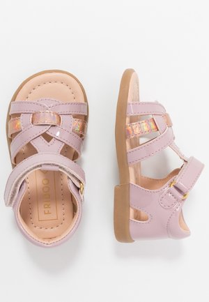 Par de sandalias de color rosa claro para niños pequeños con tiras iridiscentes, cierre de velcro en el tobillo y suelas de goma color tostado, vistas desde arriba y de lado.