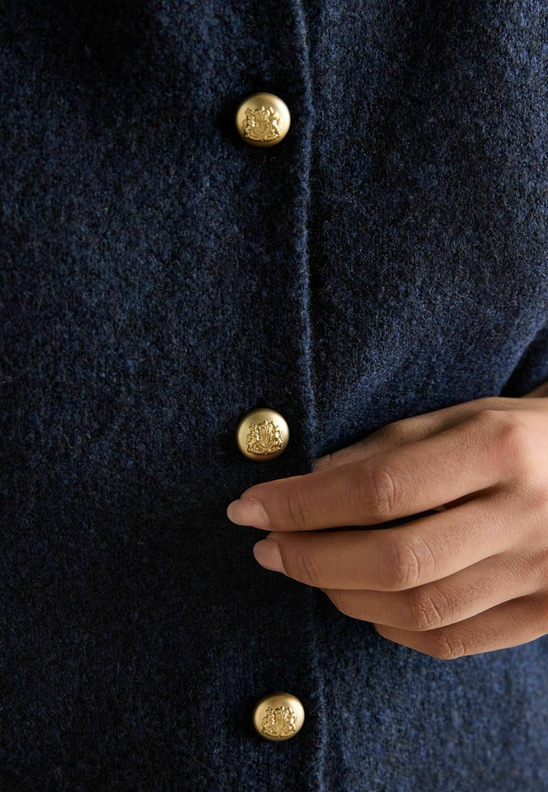 Marineblauer Wollmantel mit auffälligen goldenen Knöpfen mit geprägtem Detail, der eine glatte Textur und ein strukturiertes Design aufweist.