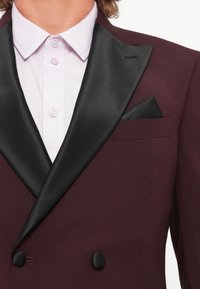 Burgundy double-breasted blazer with black satin lapels, featuring a chest pocket and a folded black pocket square, worn over a light pink shirt.