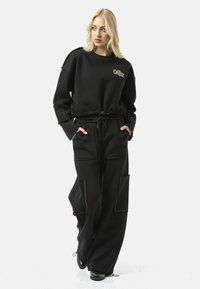 Zwarte sweatshirts met logo, voorzien van een losse pasvorm en elastische taille. Zwarte broek met meerdere zakken en contrasterende rode stiksels.