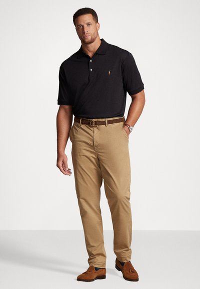 Μαύρο πόλο μπλουζάκι, μπεζ καμπάνα, καφέ ζώνη και καφέ λόφερ. Η μπλούζα διαθέτει λογότυπο μικρού μεγέθους; τα παντελόνια έχουν κανονική γραμμή με λεία υφή.