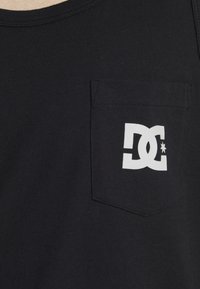 Zwart katoenen tanktop met een borstzak met een wit DC-logo, ronde halslijn en zachte textuur.
