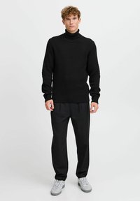 Suéter de cuello alto negro de punto con un patrón texturizado y puños acanalados, combinado con pantalones negros y zapatillas grises. Diseño simple y moderno.
