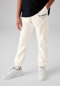 Hvide bomulds-sweatpants med elastiske manchetter, sidelommer og trykt logo-detail. Kombinationen med hvide sneakers og en sort t-shirt.