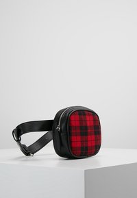 Sac en cuir noir en bandoulière de forme carrée, doté d'un panneau avant en laine à carreaux rouges et noirs, d'une fermeture éclair et d'une bandoulière ajustable.