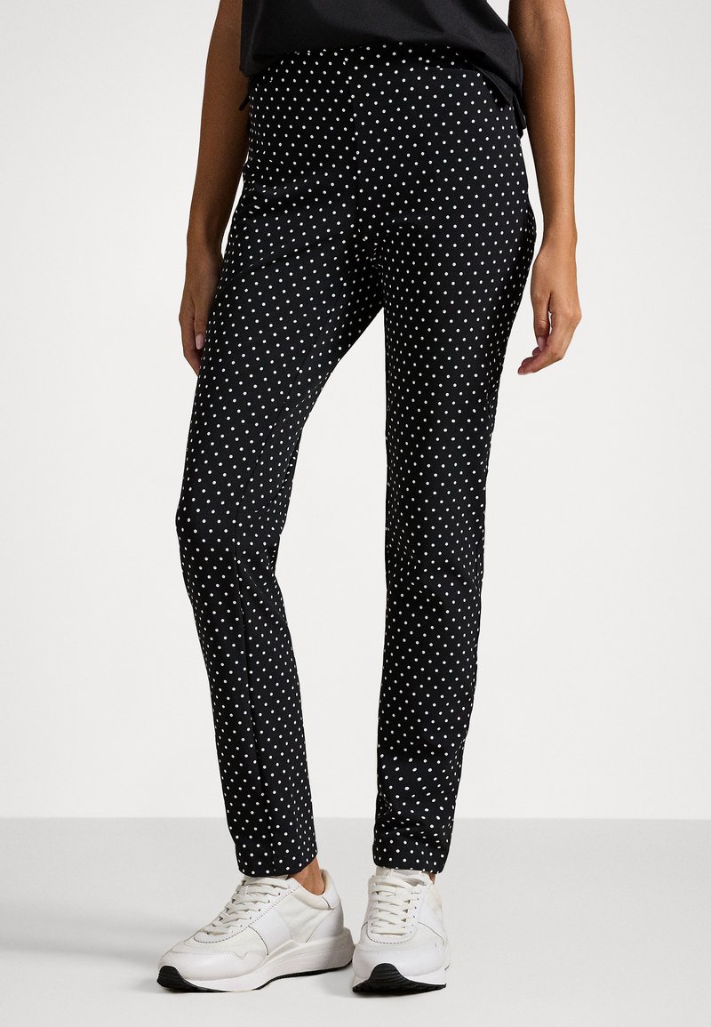 Čierne slim-fit nohavice s bielymi bodkami. Vyrobené z hladkého materiálu, s klasickým pásom a v kombinácii s bielymi teniskami.
