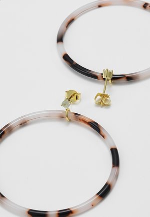 Boucles d'oreilles à clous dorés avec des anneaux circulaires à motif écaille de tortue sur fond blanc.