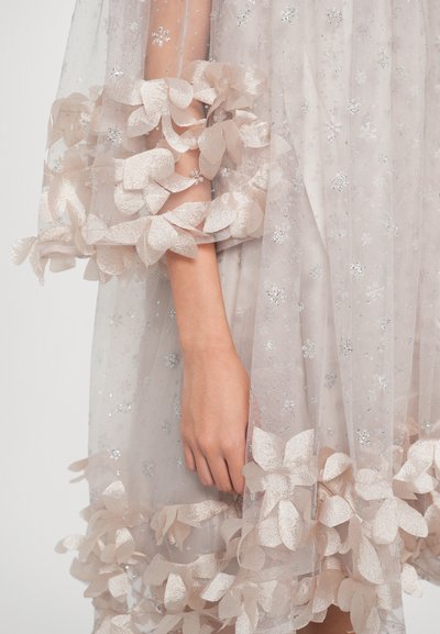 Robe légère et transparente en beige doux avec des accents pailletés. Bordure en appliqué floral aux manches et à l'ourlet. Tissu d'apparence délicate et texturée.