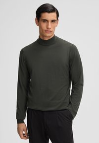 Dunkelgrüner Rollkragenpullover, lange Ärmel, aus weichem Stoff. Eng anliegende Form mit geripptem Kragen und Bündchen. Keine sichtbaren Muster oder Grafiken.